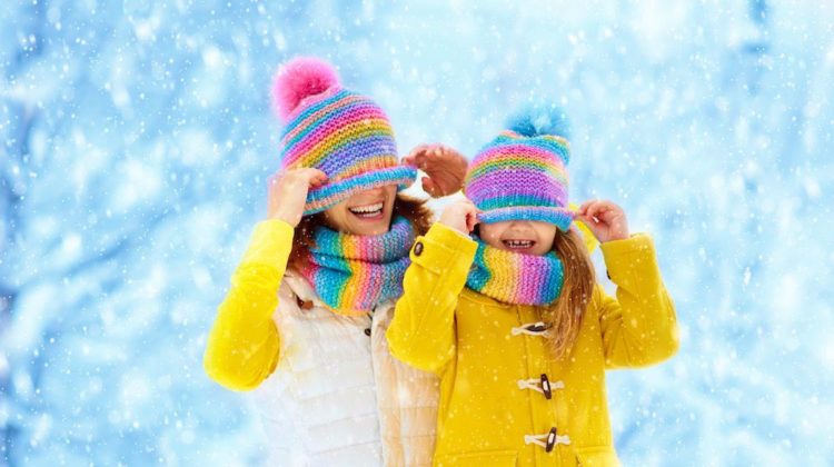 Mother and child in knitted winter hats play in snow on family Christmas vacation | Matching Cute Outfits For Girls And Moms Perfect For Christmas Parties | Featured