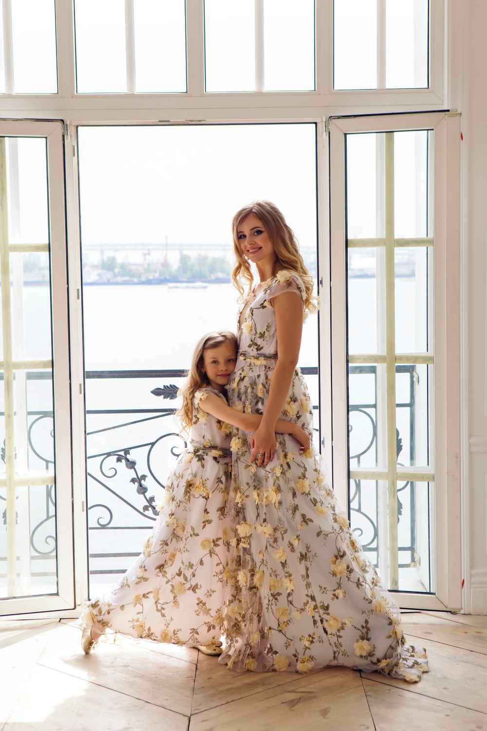 Mother and daughter in matching dresses standing at an open window on the sea background | Matching Cute Outfits For Girls And Moms Perfect For Christmas Parties
